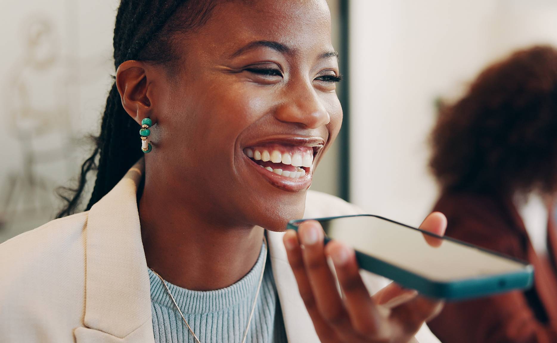 Woman smiling and holding phone up to face, talking on speaker mode.