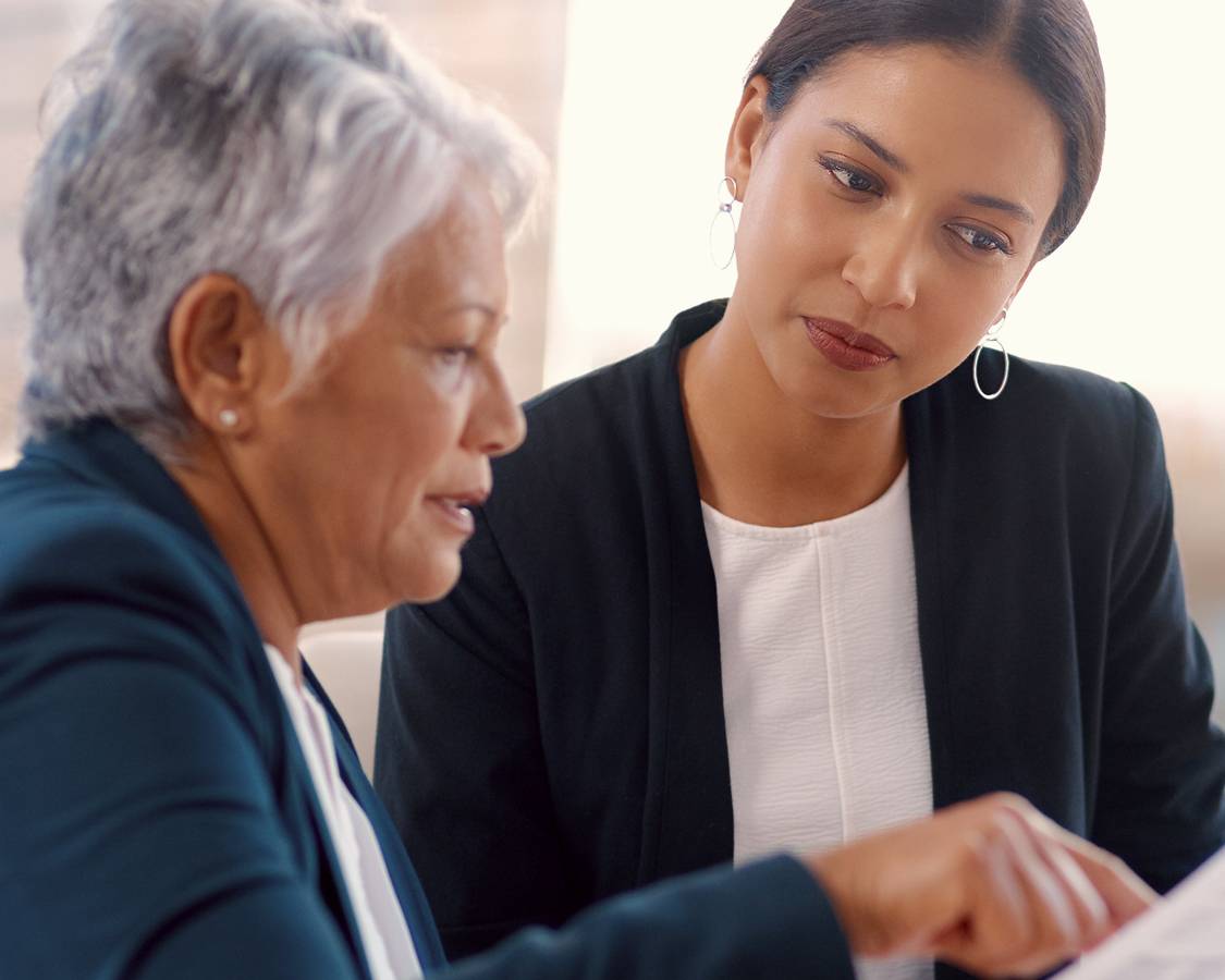 Two women in corporate environment reviewing paperwork.