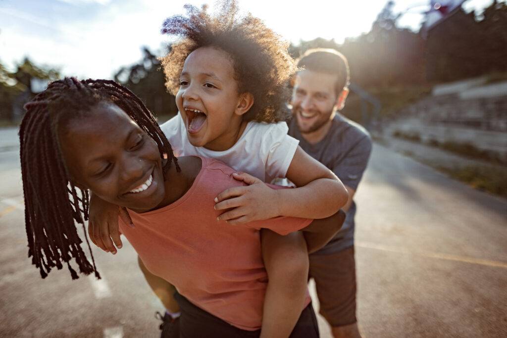 woman gives child a piggy back with man supporting from behind.