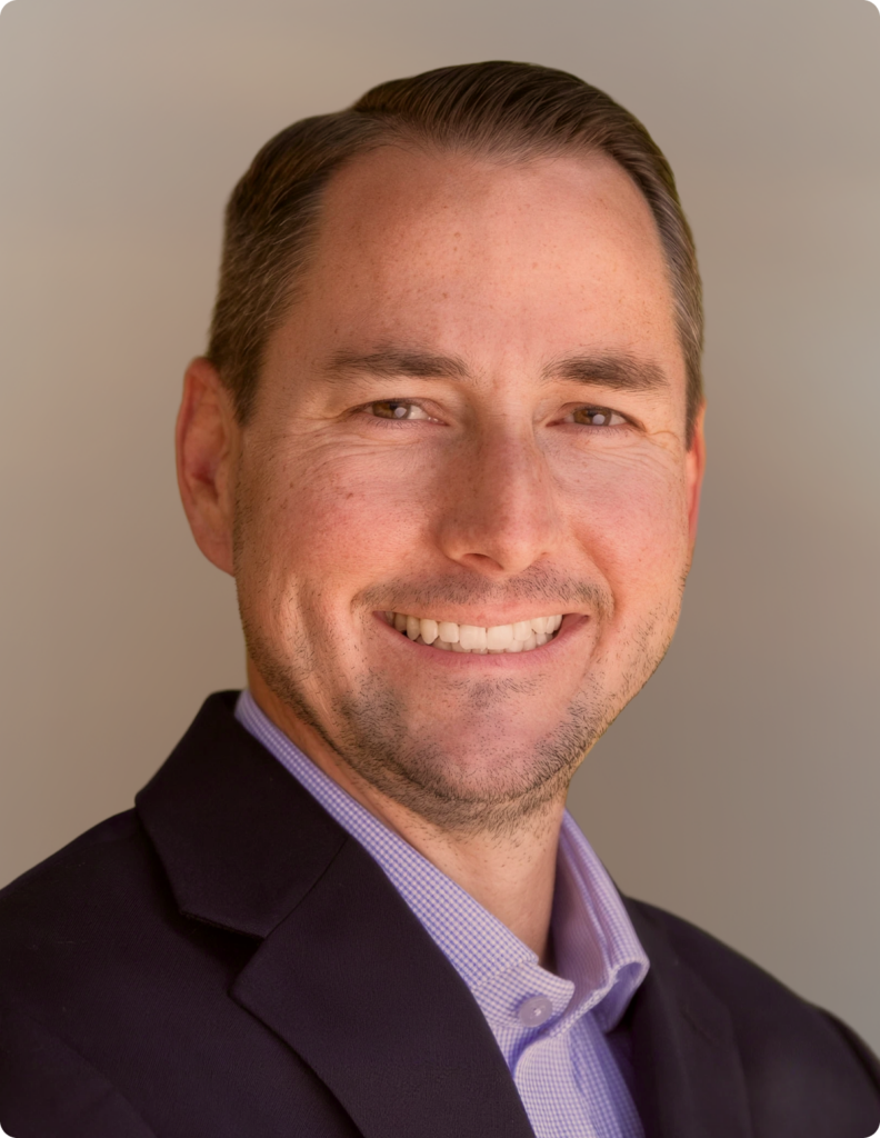 Headshot of man in front of white background, wearing blue blazer.