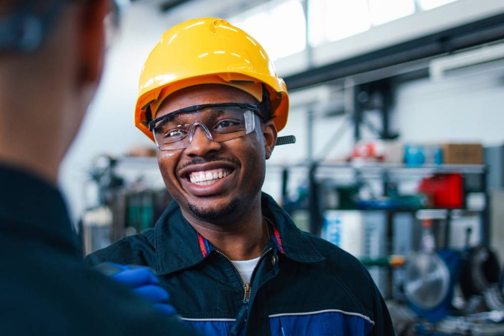 Man in hard hat and safety goggles smiles at coworker.