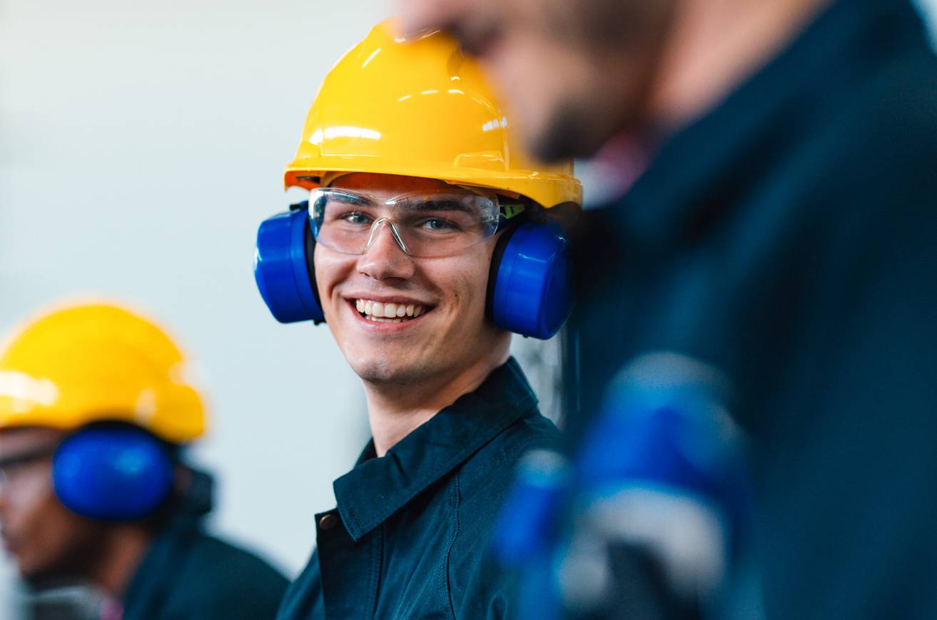 Man in hard hat and safety glasses and ear protection smiling.