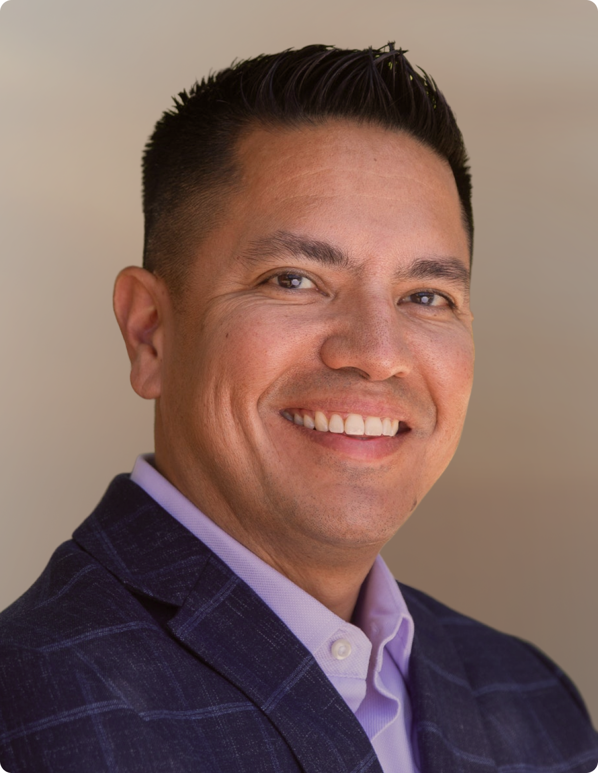 Headshot of man in front of white background, wearing blue blazer.
