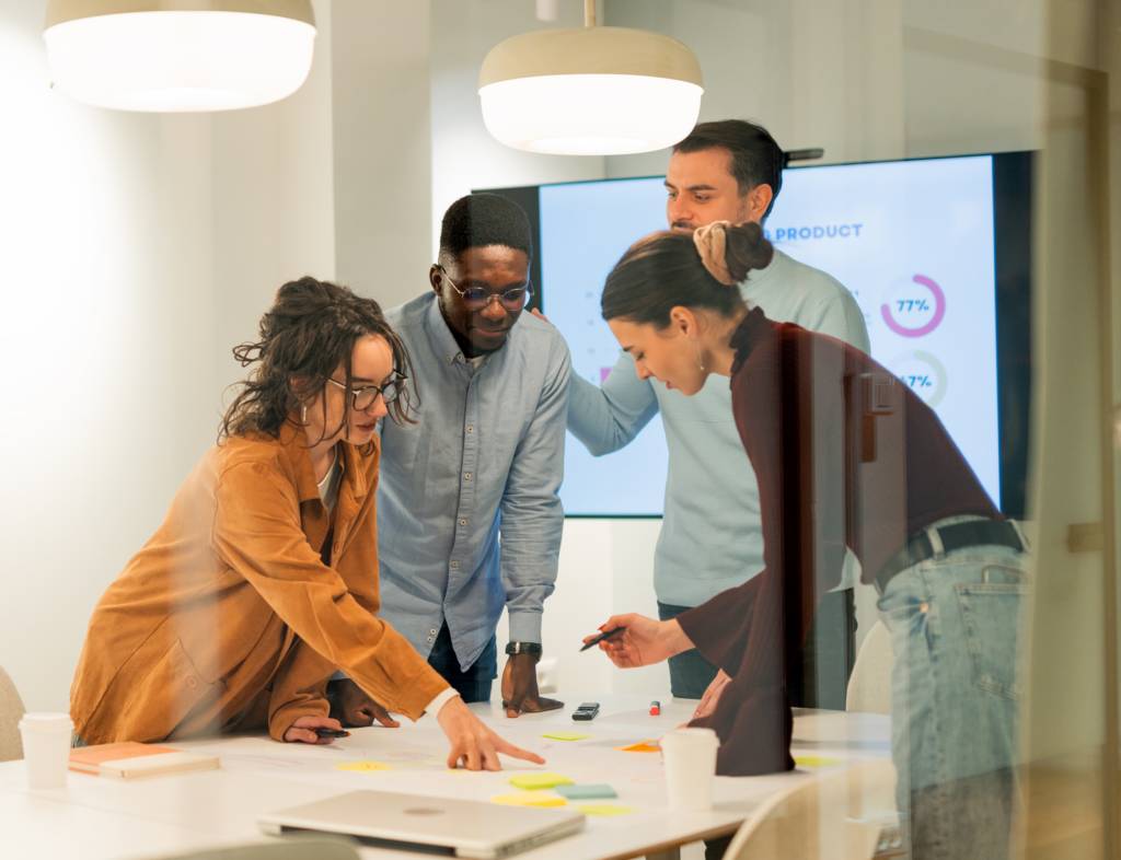 Group of employees engage around a desk, brainstorming with sticky notes.