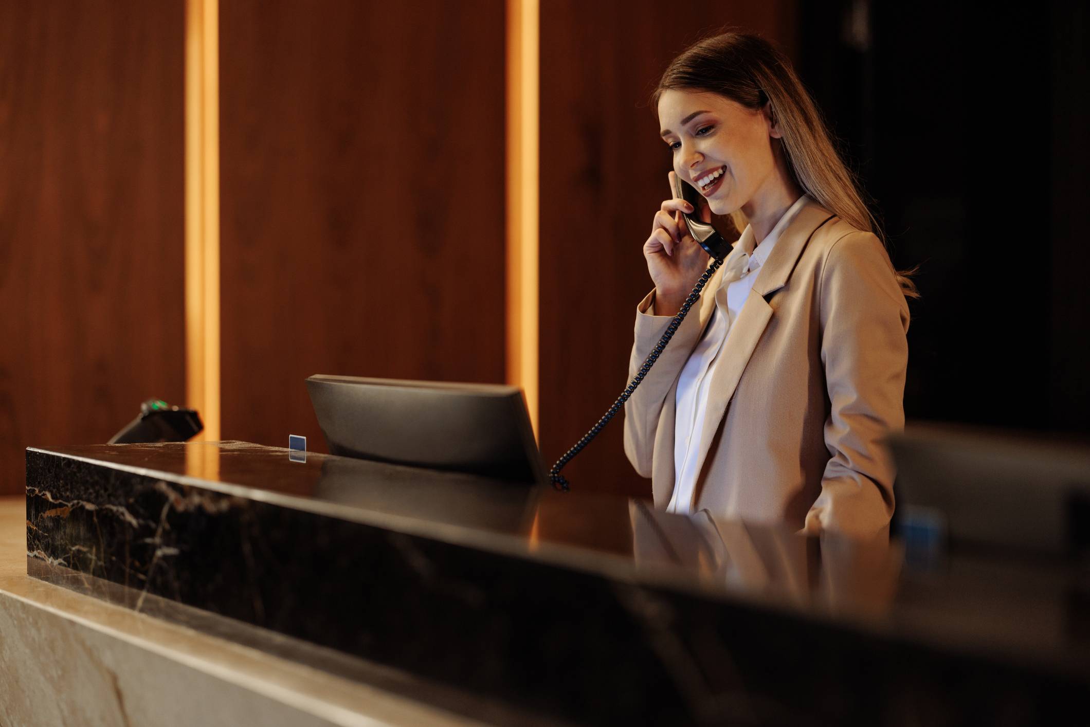 Smiling female receptionist talking on the phone while working behind the hotel helpdesk