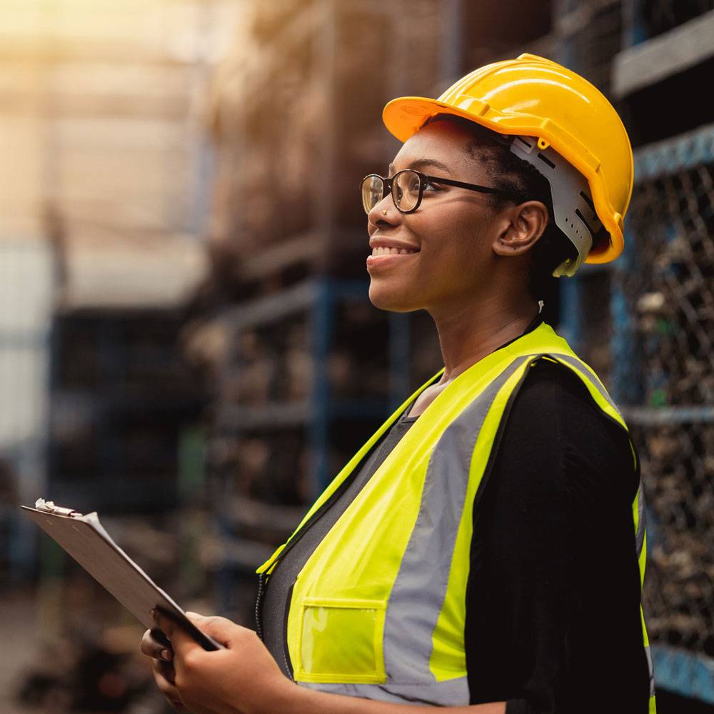 Woman in safety vest and hard hat, smiling and looking off into distance.