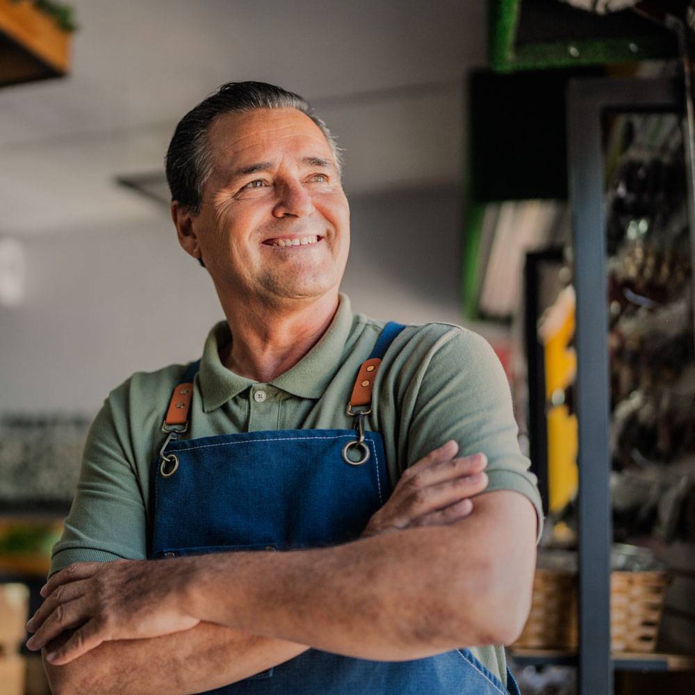 Man in apron with arms folded, smiling in front of his shop.