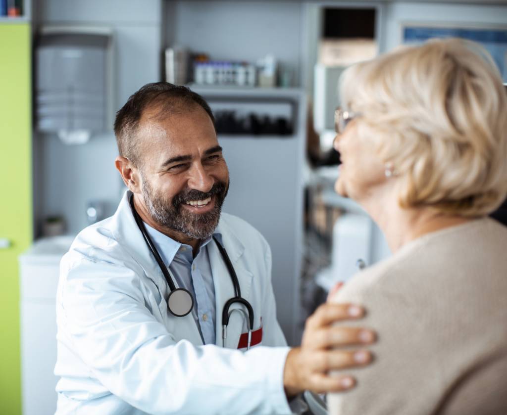 Male doctor reassuringly places arm on older woman's shoulder.