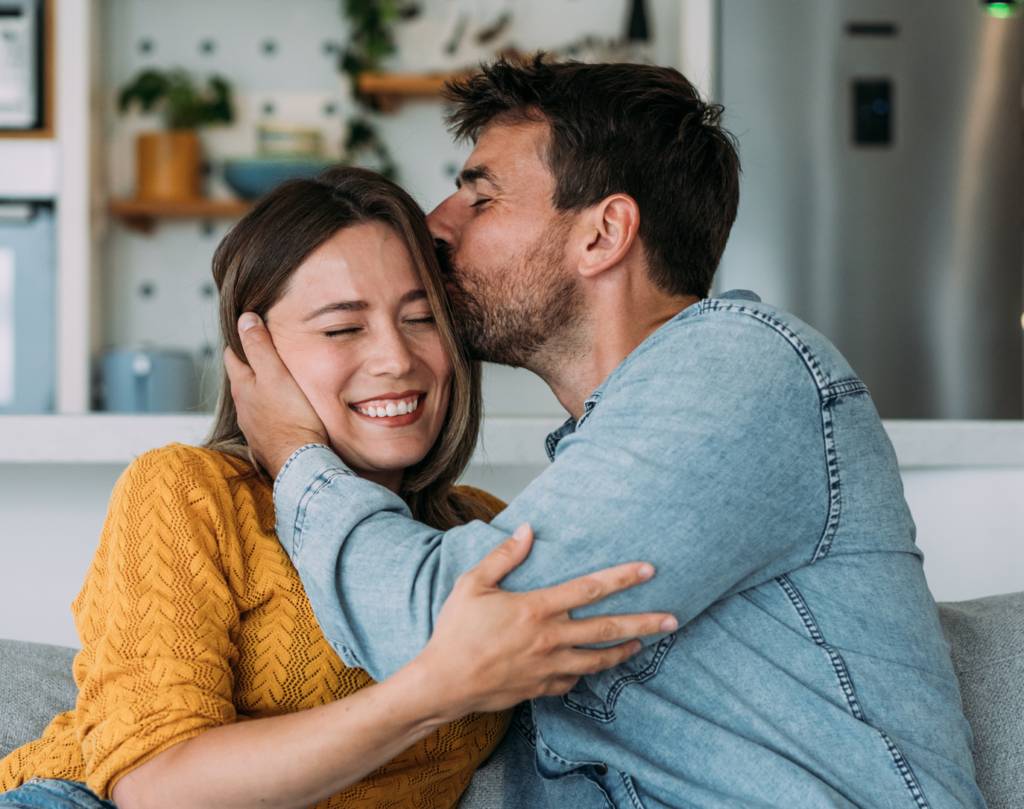 Couple embraces with man kissing woman's head.