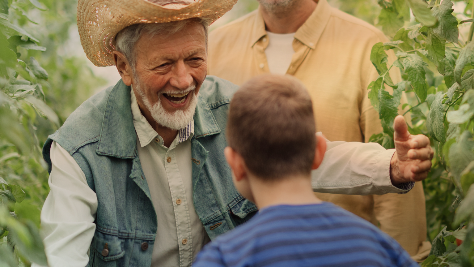 Farmer in cowboy hat reaches out to embrace child with man standing behind him.