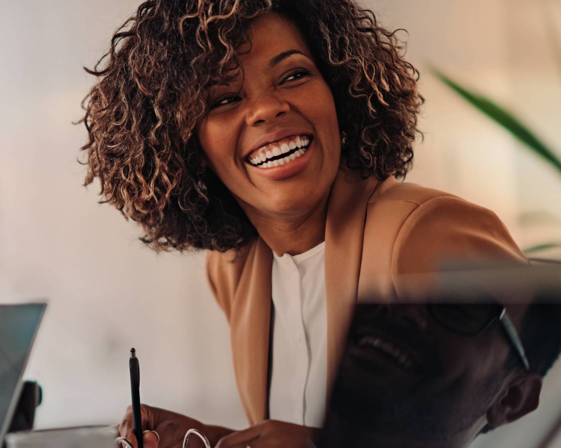 Woman smiles at desk holding a pen.