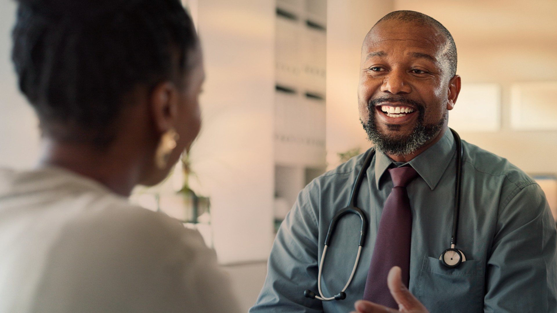 Doctor sits with stethoscope around neck talking to patient.
