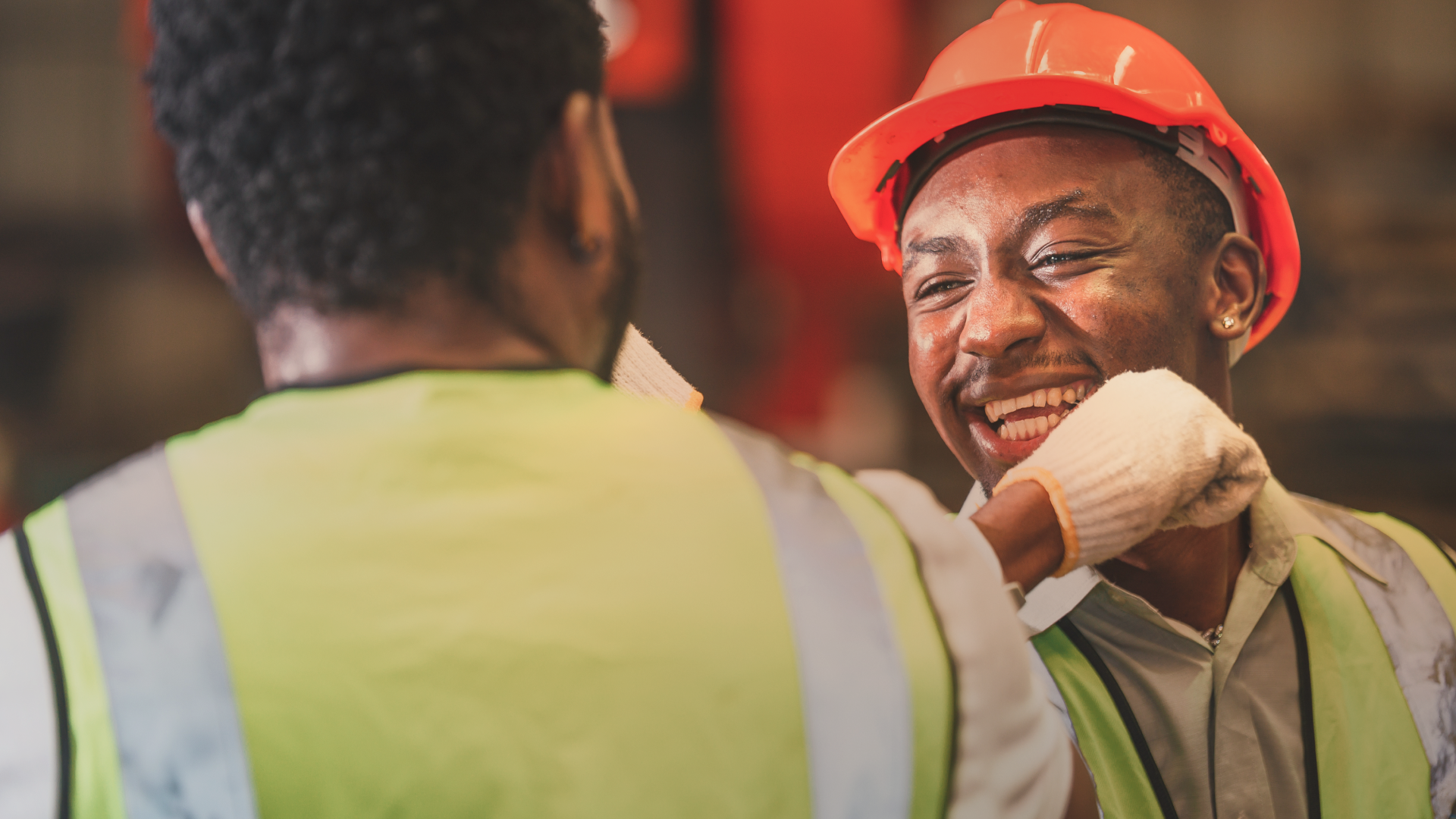 Two construction workers in hard hats and gloves bump elbows.