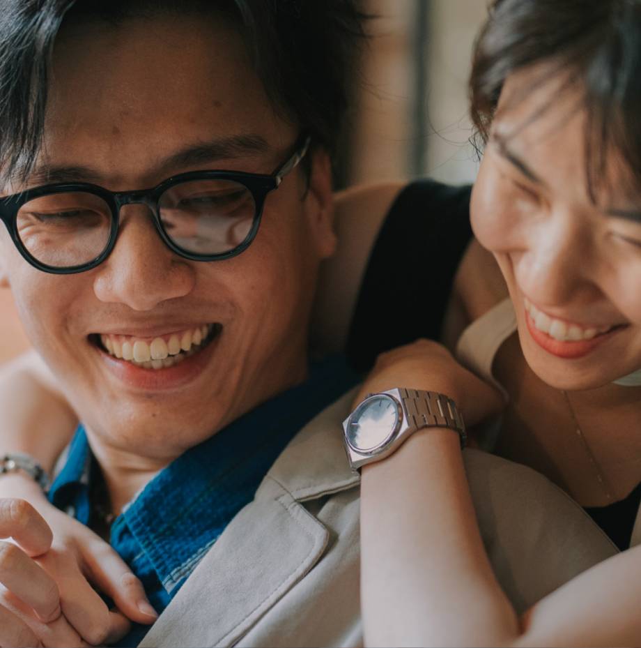 Man wearing glasses has woman behind him, wrapping arms around his shoulder.