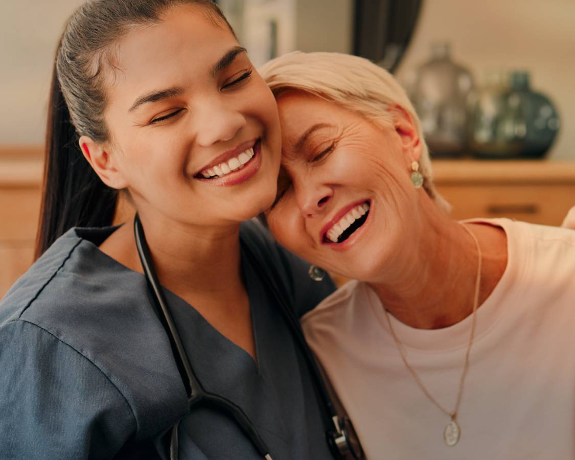 Nurse wearing stethoscope hugs older woman in a side hug.