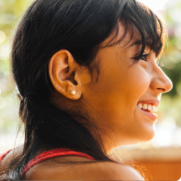Side of woman's face, smiling with sunny background.