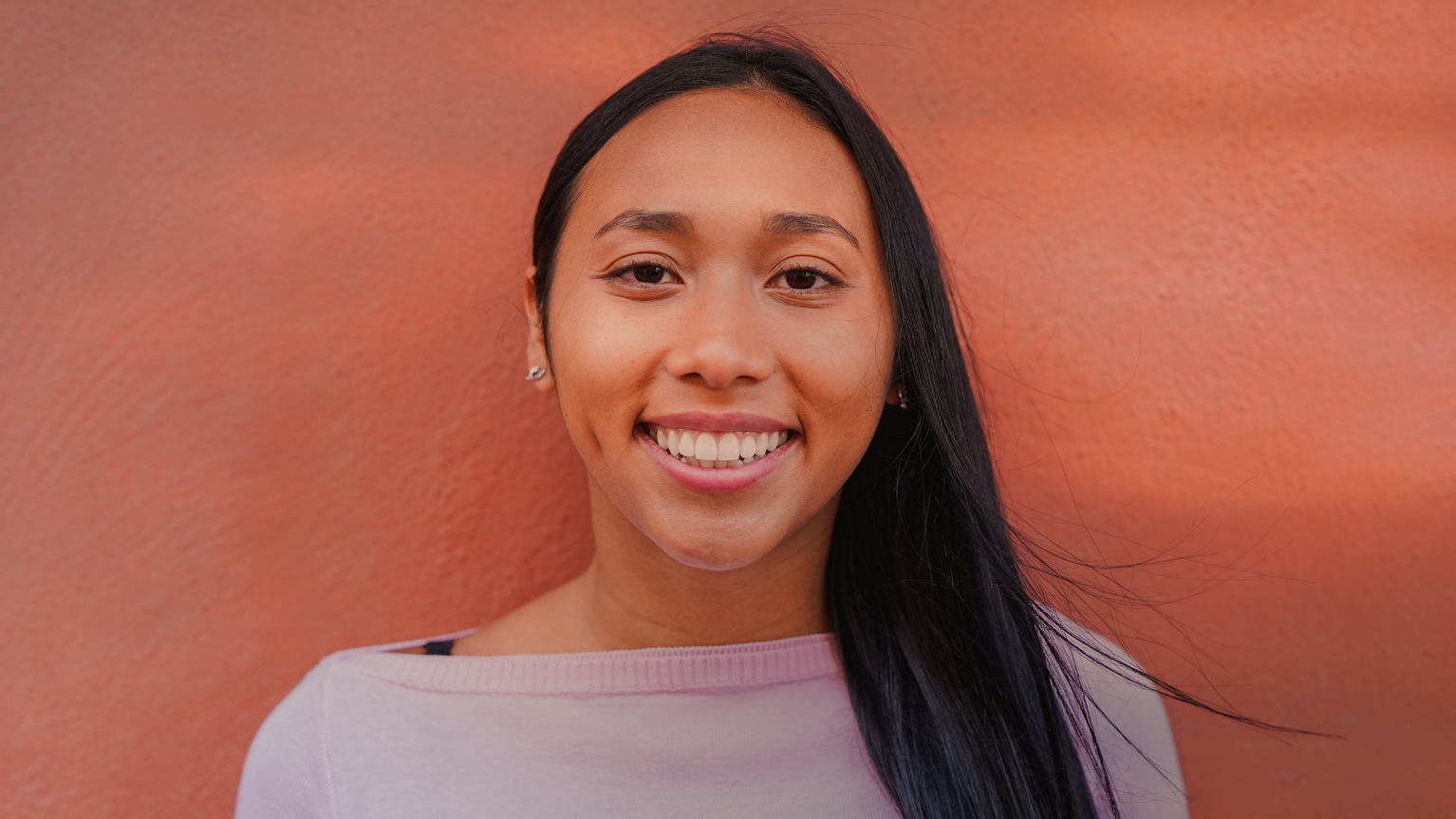 Woman in blouse smiling in front of orange wall.