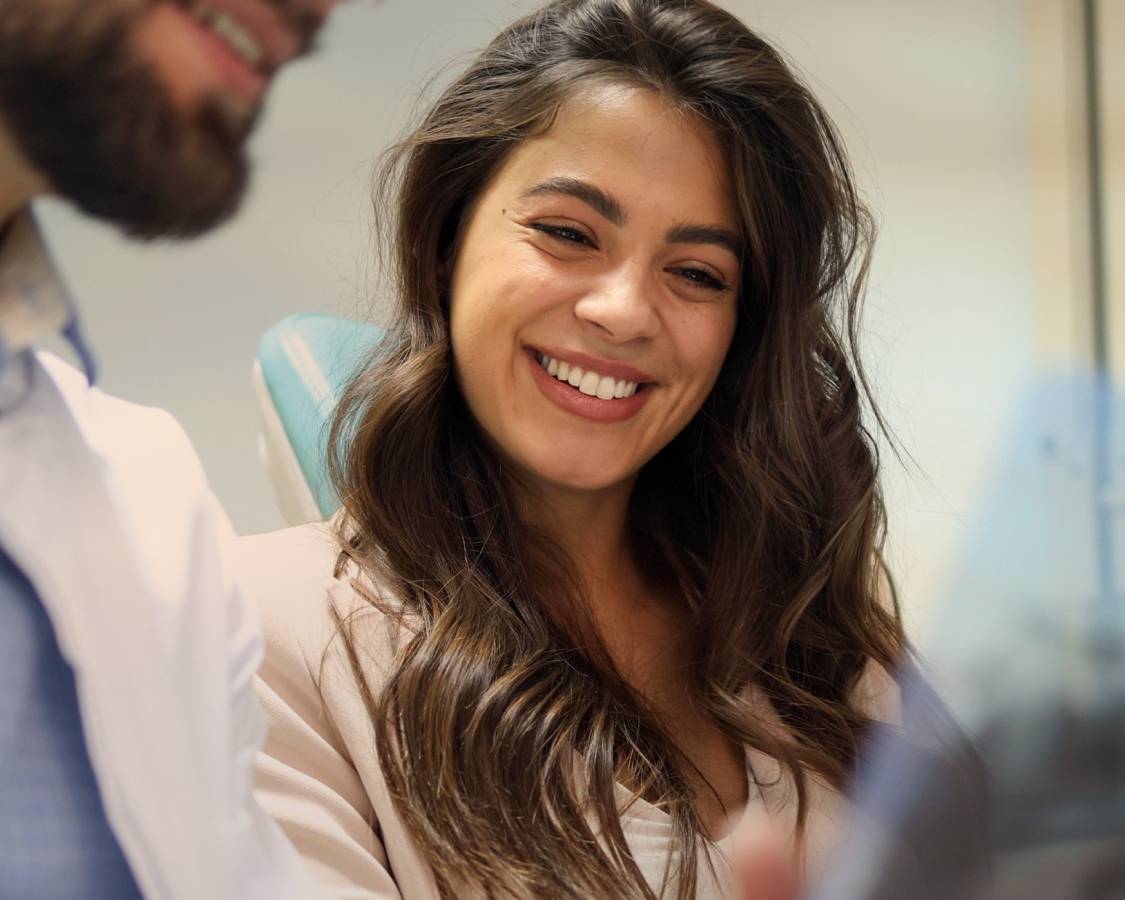 Woman sitss in chair, smiling and looking down at screen.