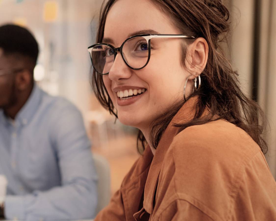 Woman in glasses and button down with hoop earrings smiling.