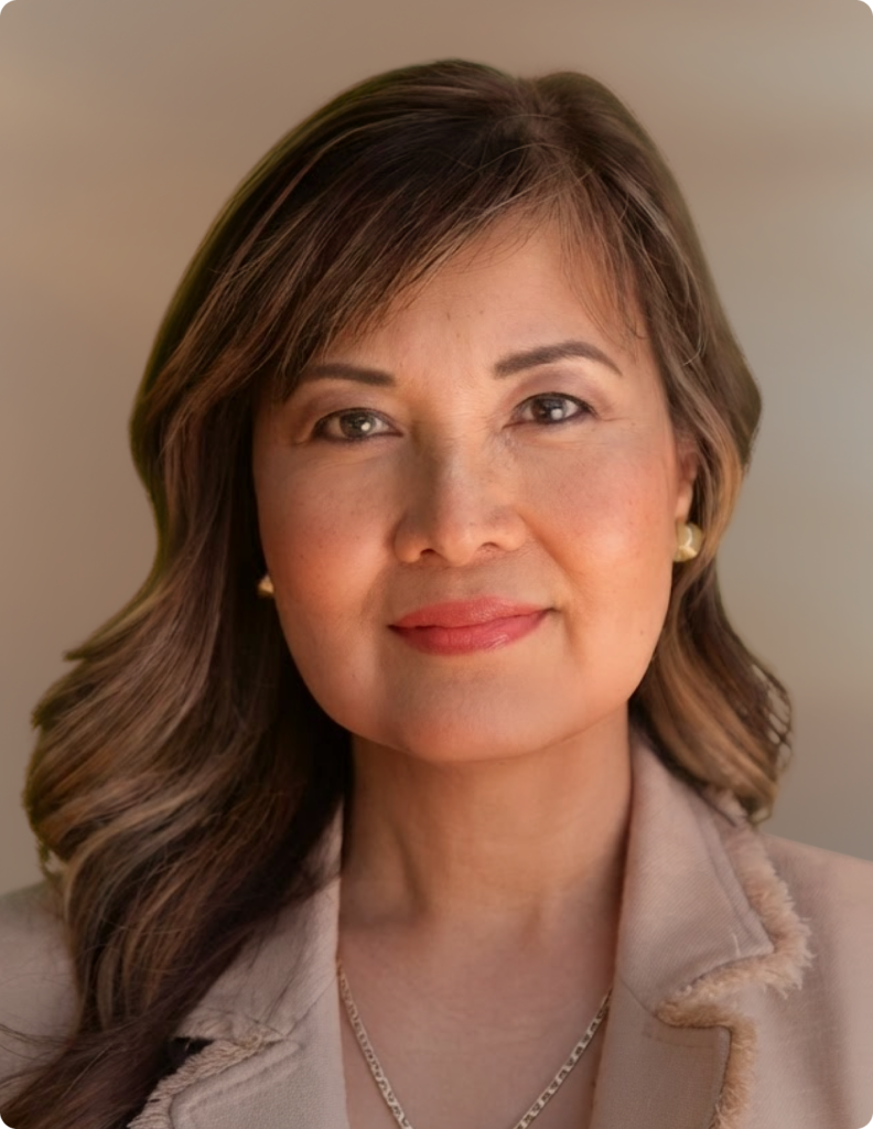 Headshot of woman in front of white background, wearing pink blazer.