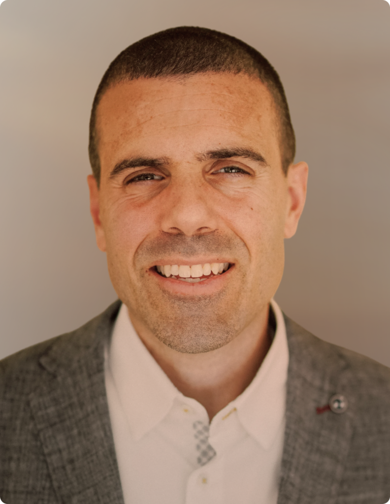 Headshot of man in front of white background, wearing gray blazer.