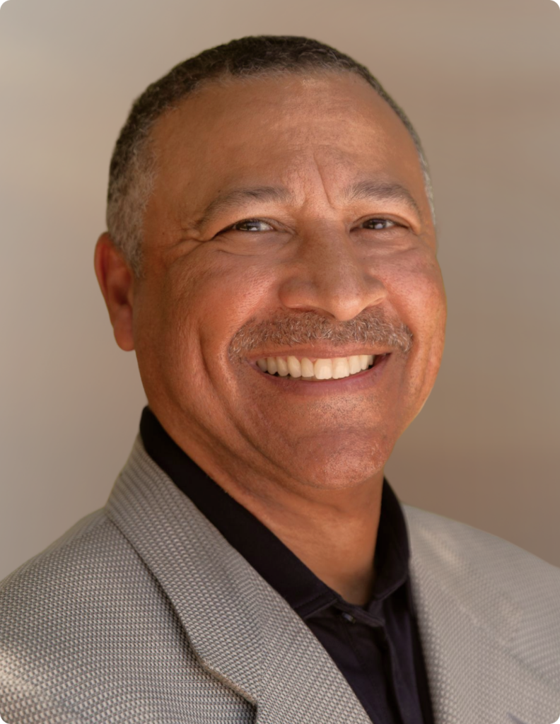 Headshot of man in front of white background, wearing gray blazer.