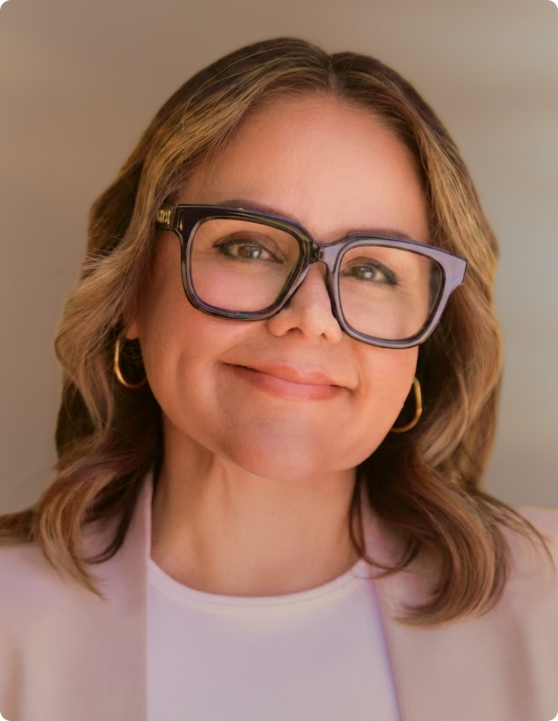 Headshot of woman in front of white background, wearing pink blazer.