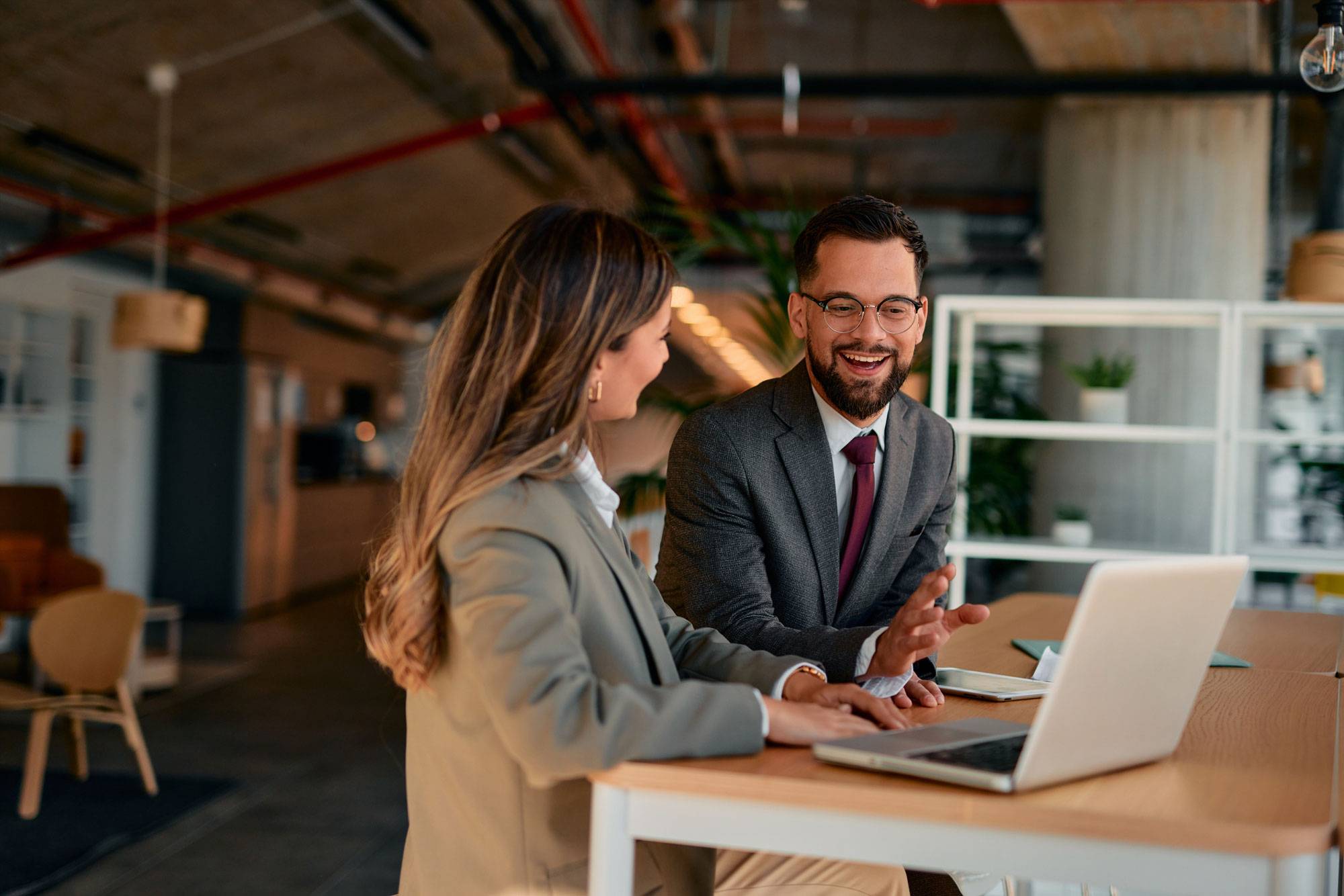 Man and woman in dress attire at standing desk, looking at laptop.