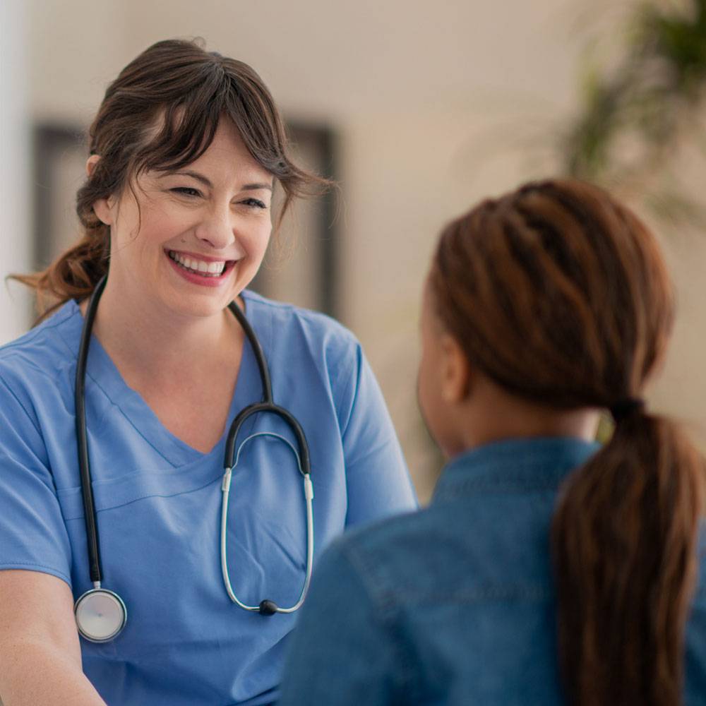 Nurse in blue scrubs and stethoscope, smiling an meeting with young patient.