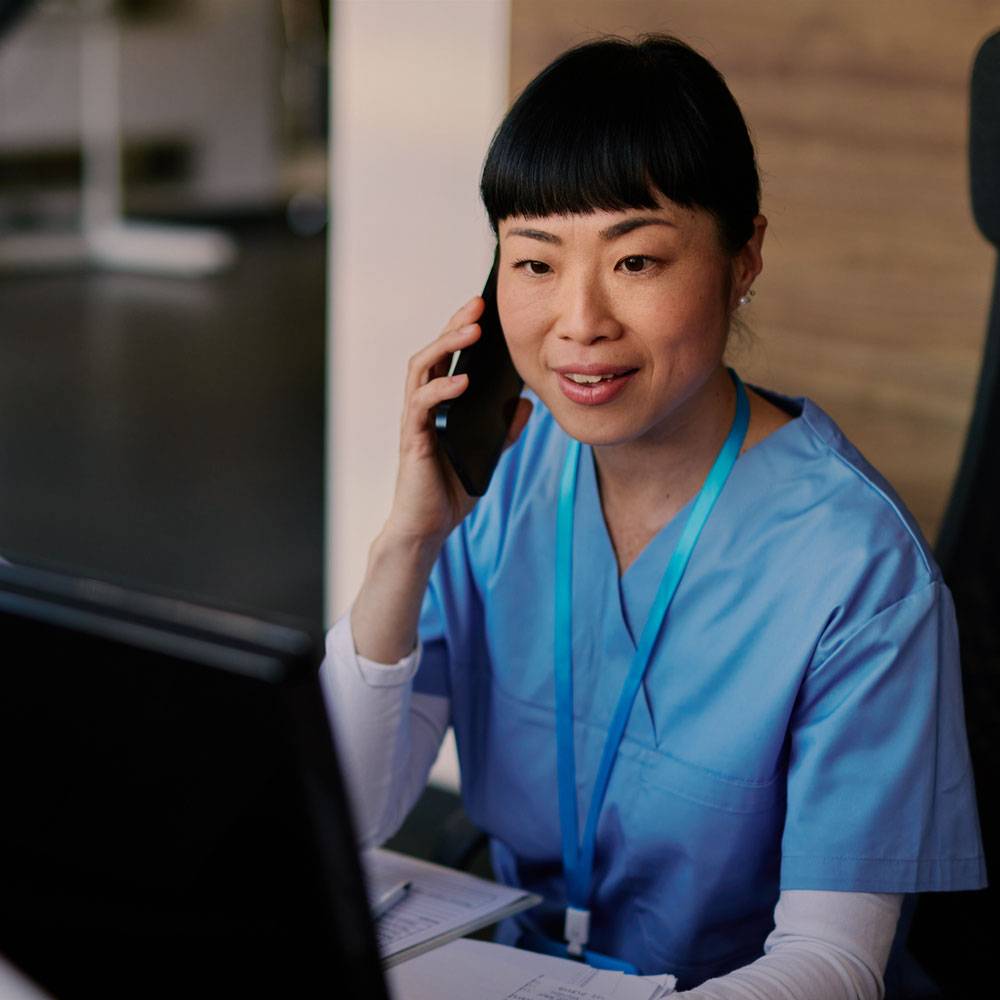 Nurse answers phone at desk while looking at computer screen.