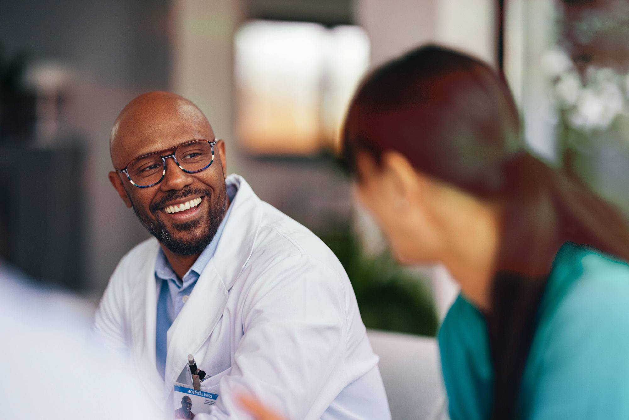 Doctor sits down in waiting room while smiling in conversation with nurse.