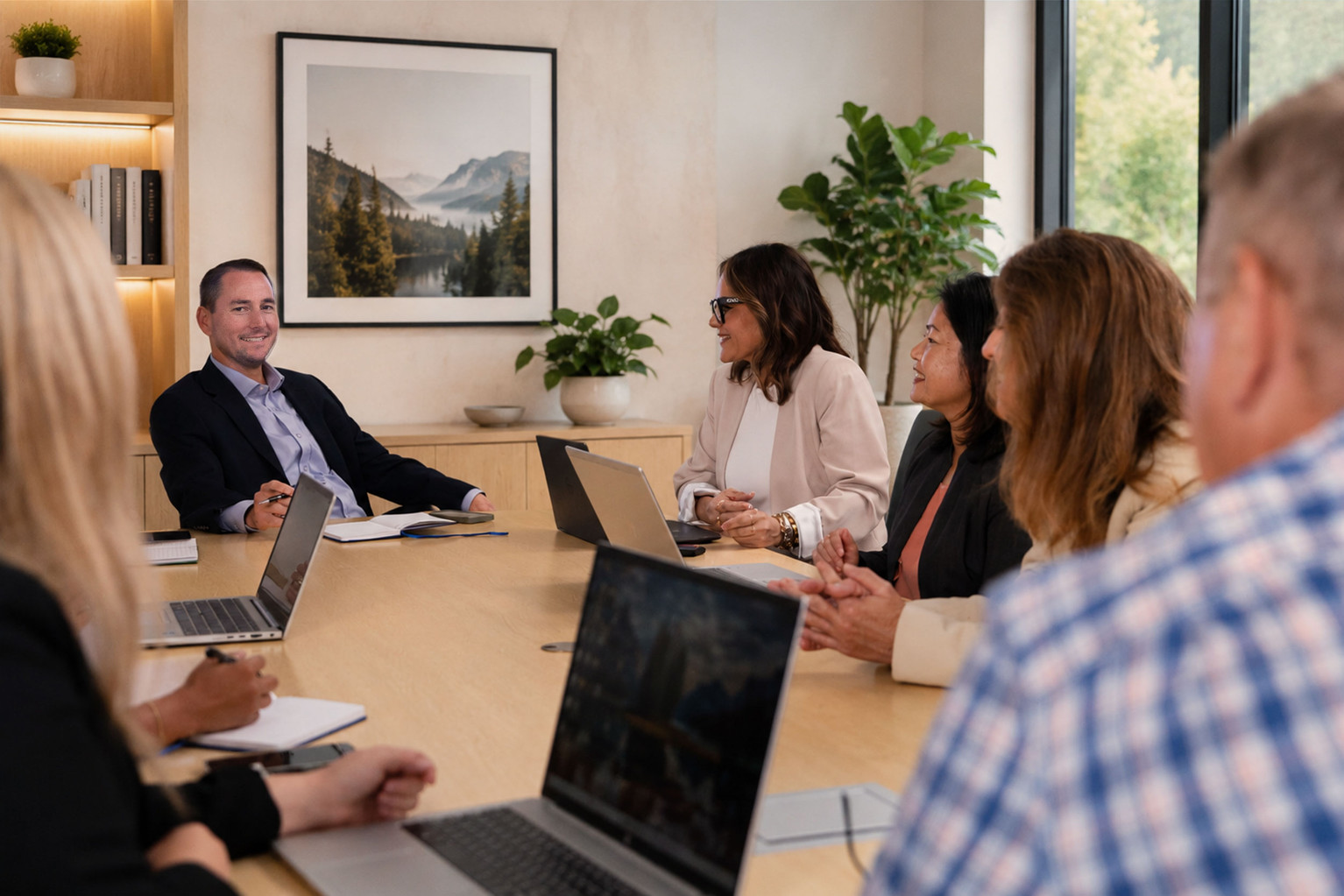 Corporate office with employees sitting around large table with laptops.