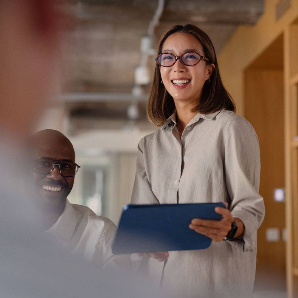 Woman standing next to man in corporate office, sharing details on her tablet.