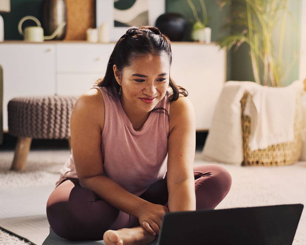 Woman sitting in yoga pants and tanktop, looking at laptop on ground.